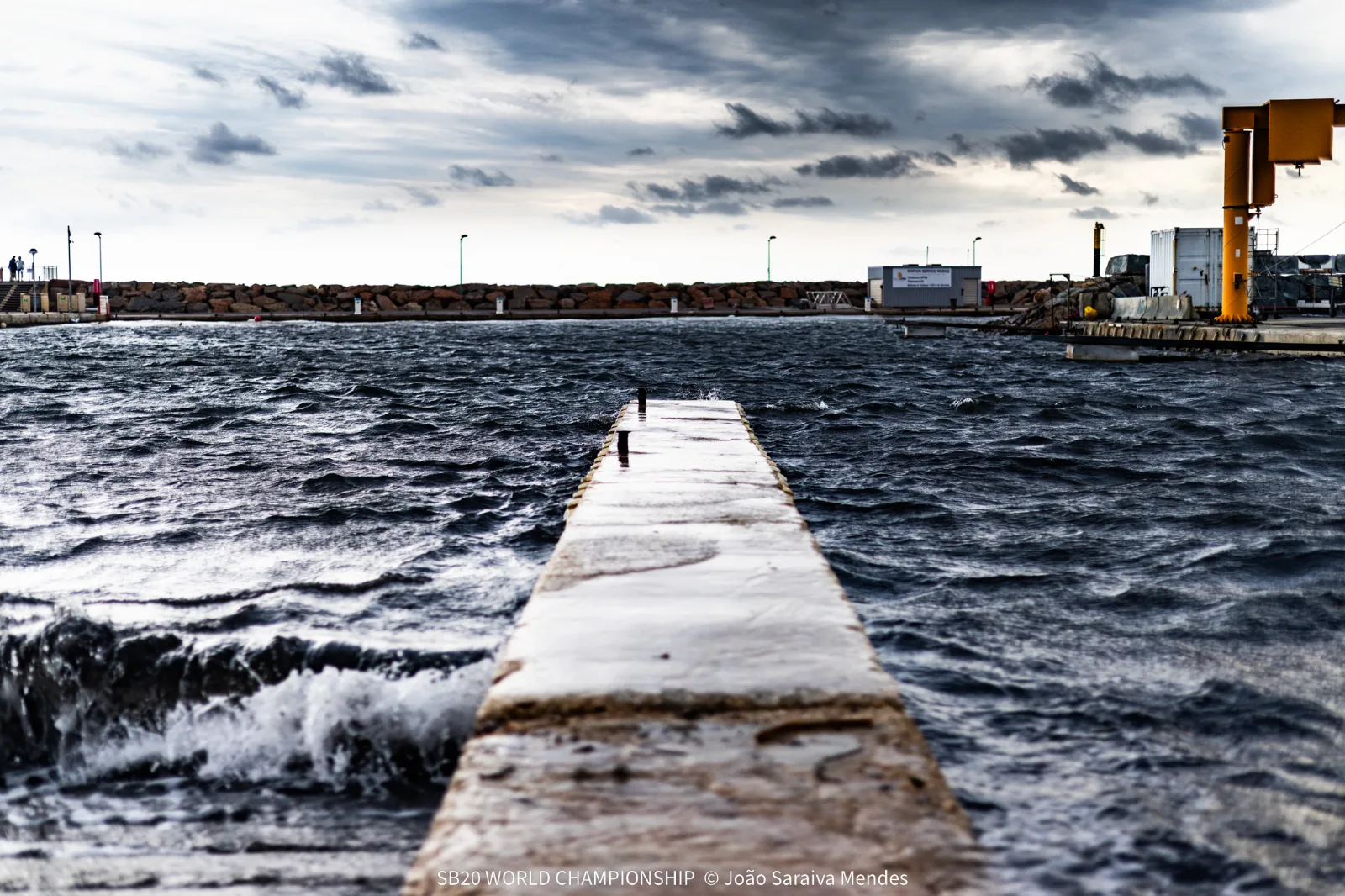 Waves breaking over the harbour wall in Hyères under dark clouds on Day 1 of the SB20 World Championship